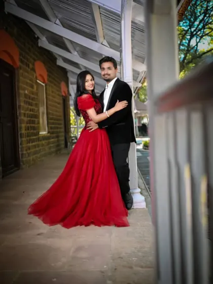 A sweet and romantic pose on a veranda. The bride's red ball gown adds a vibrant splash of color to this charming and intimate pre-wedding photo.