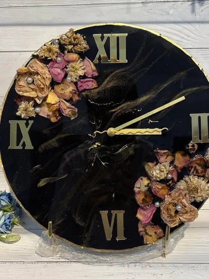 A stunning resin art clock with a black and gold marble effect. The preserved flowers are arranged on either side, creating a balanced and artistic timepiece.