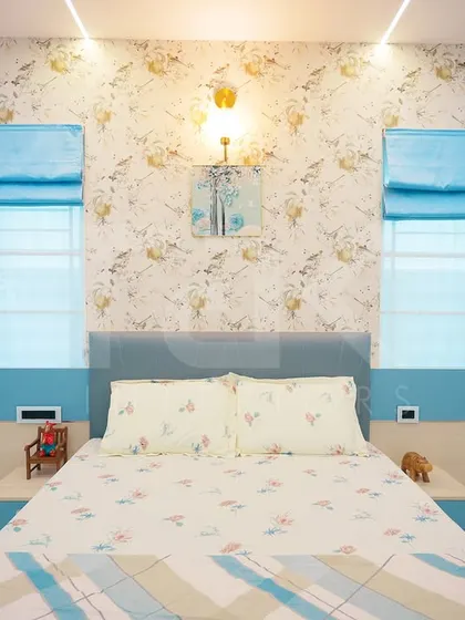 This charming bedroom features a floral wallpaper and a light blue headboard. The design is fresh and playful, with traditional wooden carvings adding a unique, personal touch.
