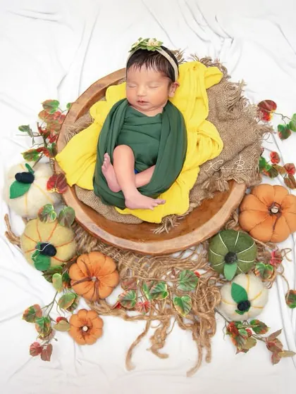 An autumn harvest theme, with a newborn nestled in a wooden bowl surrounded by colorful miniature pumpkins and gourds. The textures and colors are perfect for a fall baby.
