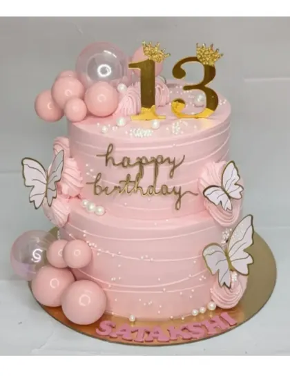 A beautiful pink two-tier cake for Satakshi's 13th birthday. This chocolate truffle cake is decorated with butterflies, bubble-like spheres, and a golden crown to mark the special teenage milestone.