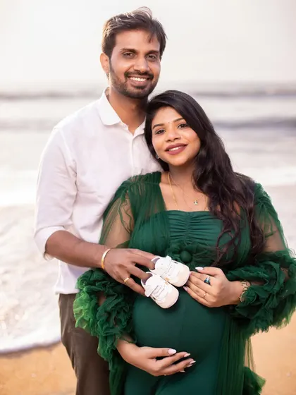 A happy couple portrait on the beach, using baby shoes as a sweet prop to announce their coming joy.