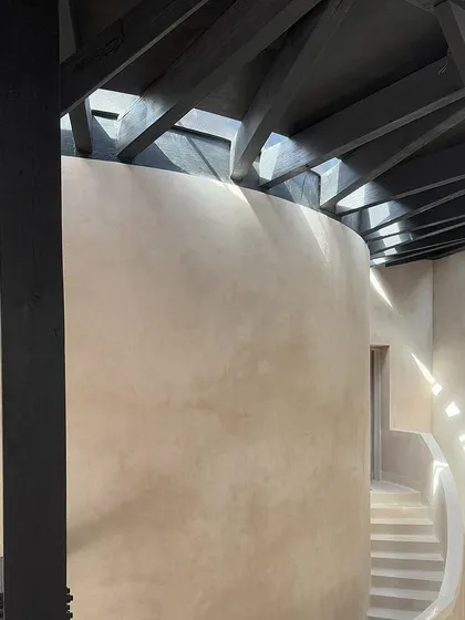 In the House of Galleries, long curvilinear skylights allow slivers of light to wash over the lime-washed walls. The charred timber rafters create a rhythmic pattern of light and shadow, adding depth and character to the space.
