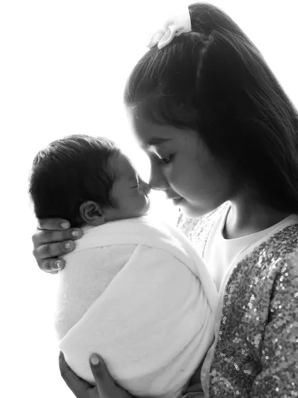 Another beautiful black and white shot capturing the gentle bond between an older sister and her newborn sibling. Her expression is full of care and wonder.