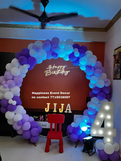 This balloon ring decor for a 4th birthday uses a bold purple and white color scheme. The setup includes a 'Happy Birthday' neon sign, the child's name in marquee letters, and a light-up number '4'.