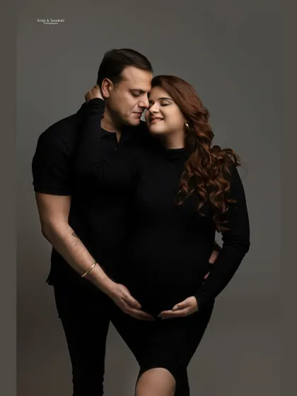 An intimate portrait of togetherness. Dressed in matching black, this couple shares a quiet, loving moment, their hands gently cradling the baby bump.