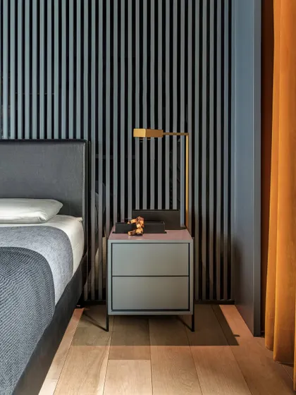 A detail of the bedside in the 'Wedged Haus' son's bedroom. The headboard wall of grey ribbed wooden slats and smoked glass creates an illusion of depth, while an ochre yellow curtain adds a block of contrasting color.