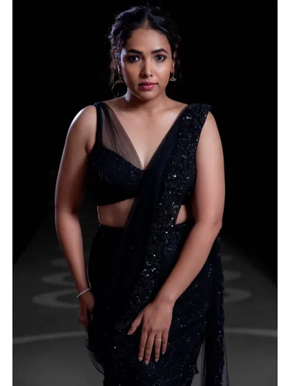 A striking portrait of Anupama Gowda. The gown features a modern blouse with a sheer V-neck panel, adding a touch of allure to the all-black ensemble.