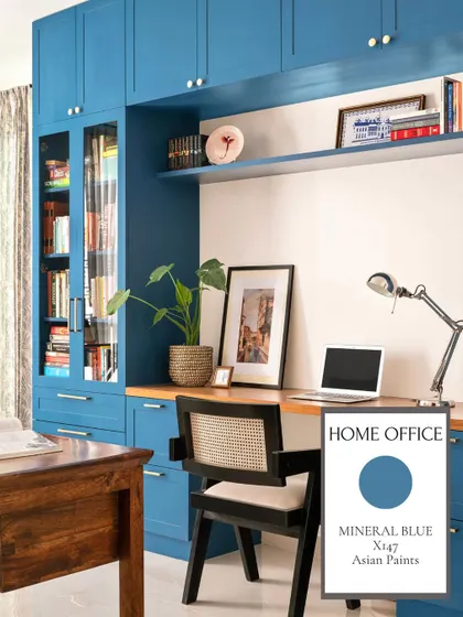 This home office features bold 'Mineral Blue' cabinetry, creating an energizing and inspiring environment for work. The wood desk and rattan chair provide a natural, grounding contrast.