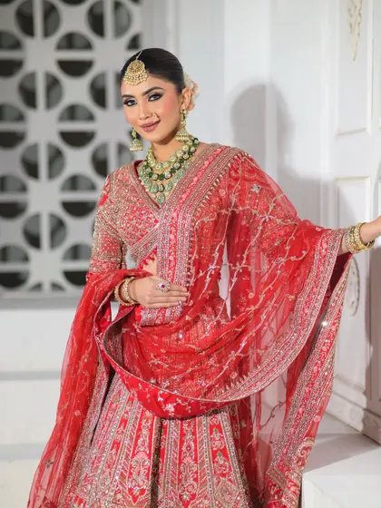 A full-body shot of the bride in a stunning red lehenga, smiling brightly. The makeup is bold enough to stand out yet elegant enough to feel timeless.