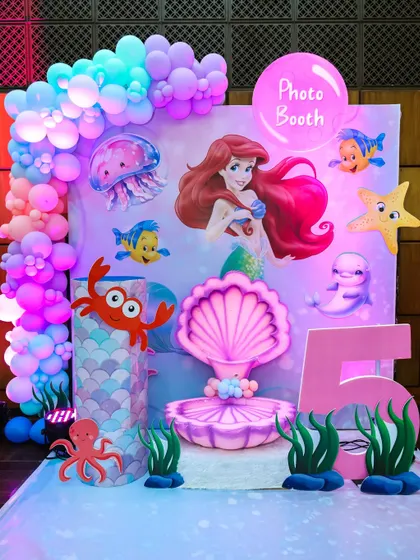 An enchanting 'Under the Sea' photo booth for a Little Mermaid party, with a clamshell seat, character cutouts, and bubble-like balloons.