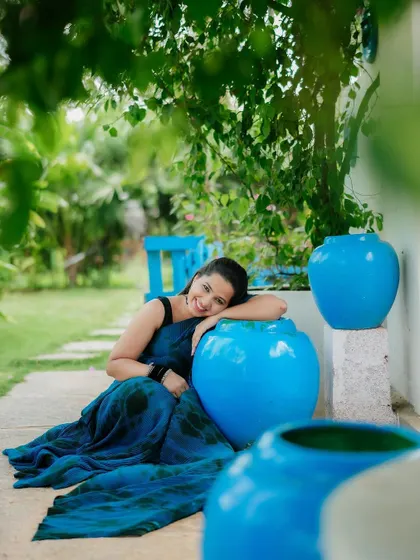A lovely solo portrait of the bride-to-be, smiling brightly. The vibrant blue pots complement her saree, creating a colorful and cheerful composition.