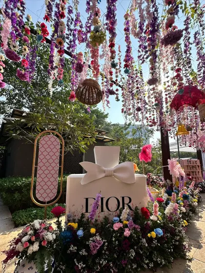 A wider view of the Dior perfume bottle installation, showing the hanging floral ceiling and the overall lush, garden-party atmosphere of the event.