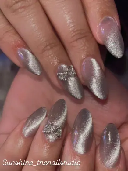 A mesmerizing silver cat eye effect on almond nails, accented with 3D rhinestone bows.
