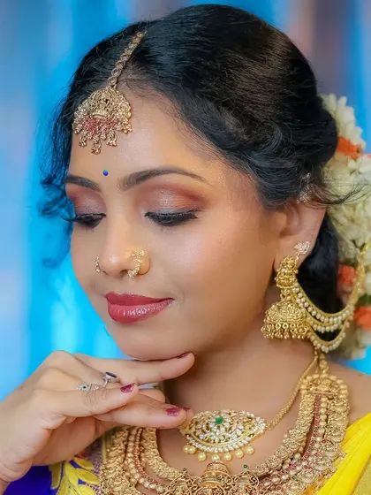 A close-up bridal portrait showing off the flawless makeup and traditional gold jewelry. The soft blue and yellow background adds a touch of color to this elegant shot.