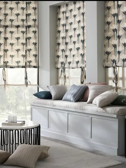 A bright sunroom featuring a window seat with striped cushions and floral roman blinds. This image shows how different patterns from the same collection can be mixed and matched.