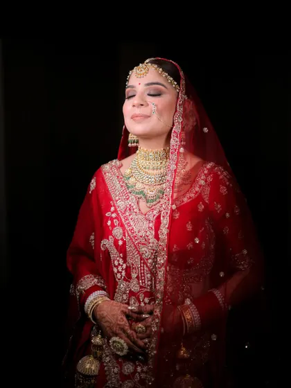 A moment of pure bridal bliss. The makeup is designed to look serene and glowing, with highlighted cheekbones and soft eye makeup that catches the light beautifully against the dark background.