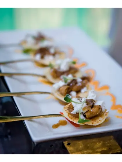 An elegant canapé served on a golden spoon, featuring a mini pancake topped with a savoury mushroom ragout and cream.
