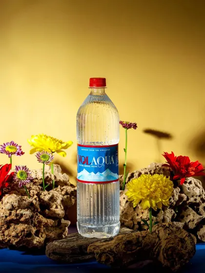 An artistic and conceptual shot of a Volaqua bottle surrounded by fresh flowers and natural stones. The composition feels like a small, natural oasis, reinforcing the water's purity.