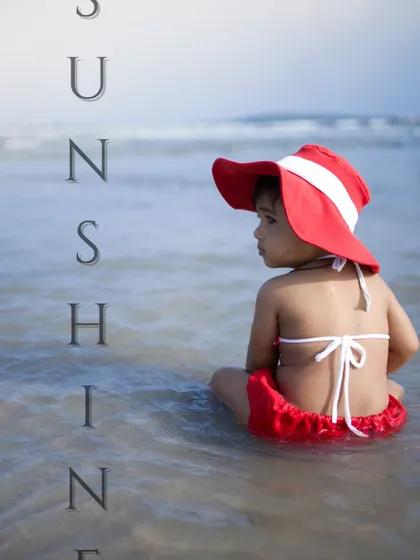 A pensive moment for this little girl sitting in the shallow water at the beach. The red hat adds a beautiful pop of color against the serene ocean backdrop.