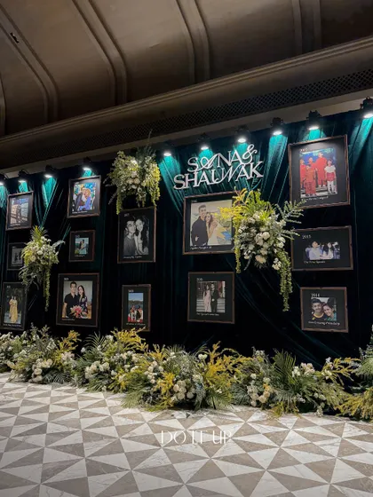 A full view of the memory wall, showcasing the couple's journey through photographs. The wall was flanked by lush arrangements of white and green florals, tying it into the overall elegant theme of the sangeet.