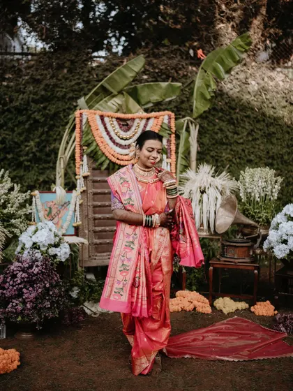 A full-length portrait of a bride in her pink nauwari saree, set against a backdrop of traditional decor. This shot captures the complete bridal look and the festive atmosphere.
