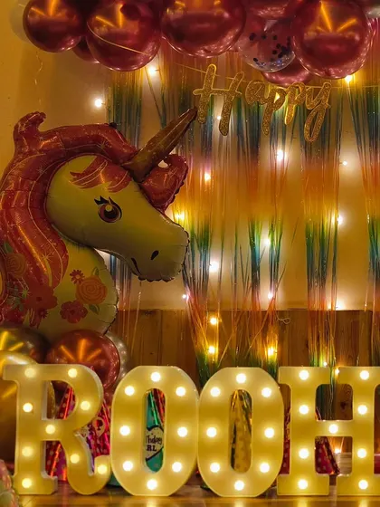 A close-up of Roohika's name in marquee letters against a backdrop of a unicorn balloon and shimmer curtain. The warm lights add a cozy and magical feel to the decor.