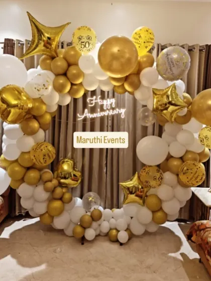 An elegant 50th anniversary celebration in classic gold and white. This decor includes a full balloon ring, a 'Happy Anniversary' neon sign, and star-shaped foil balloons, making the golden jubilee feel extra special and grand.