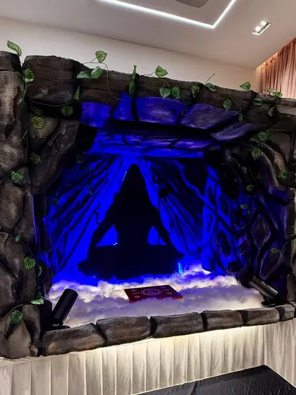 A unique cave themed Ganpati decoration for a home. The setup uses faux rock panels, dramatic blue lighting, and artificial fog to create a mystical Amarnath cave effect.