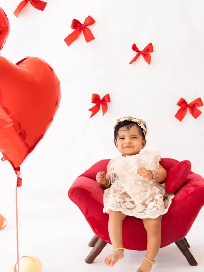 A smiling baby girl in a red armchair, surrounded by red bows. This simple setup is perfect for capturing sweet holiday portraits.