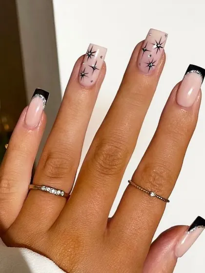 A glamorous 'starburst' design on long coffin nails, with black French tips and accent nails featuring scattered, sparkling stars.