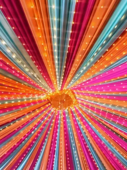 A vibrant ceiling canopy with bright pink, orange, and blue drapes, all lit up with fairy lights. This is perfect for a high-energy Sangeet night.