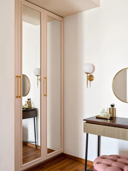 This elegant dressing corner features a slim console table and mirrored wardrobe doors in a soft blush tone. The brass handles and wall sconce add a touch of glamour and sophistication.