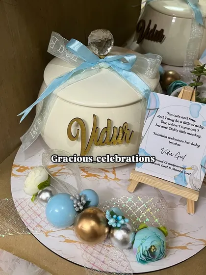 A close-up of our personalized baby announcement platter. This one features an elegant ivory handi for sweets like rasgulla or panjeeri, a live plant, and a custom card on a mini easel, all personalized with the baby's name.