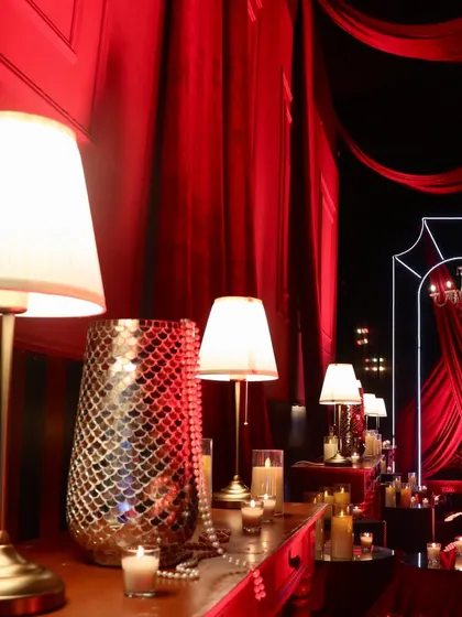 A detailed view of the decor, with warm table lamps, pearl strings, and mosaic vases set against dramatic red draping.