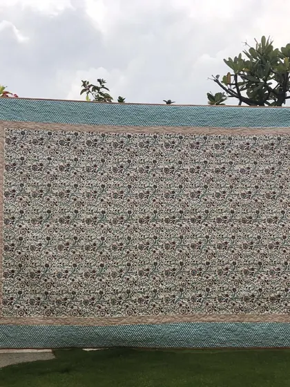 A large quilt with a classic floral print and a simple, elegant border, displayed outdoors.