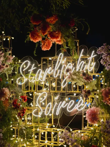 A custom neon sign reading "Starlit Soiree," nestled within a golden structure and surrounded by florals, creating a perfect, instagrammable branding moment for the event.