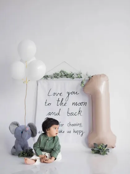 Before the cake smash begins. A calm, sweet portrait celebrating one whole year, with a simple and elegant setup featuring a "Love you to the moon and back" banner.