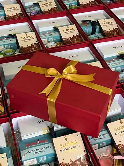 Another angle of our bulk hamper preparation, showing the scale of our operations. A finished red gift box is placed amidst rows of others ready to be packed.