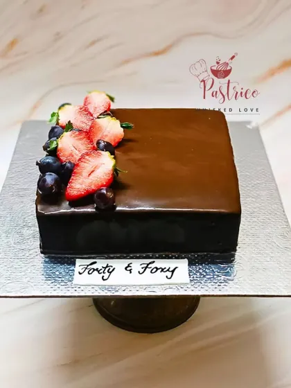 An eggless Belgian chocolate truffle cake with a flawless mirror glaze, topped with fresh strawberries and blueberries.