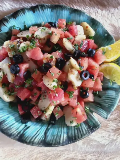 A refreshing watermelon and water chestnut salad with black olives and a lemon garnish, served in a leaf-shaped bowl.