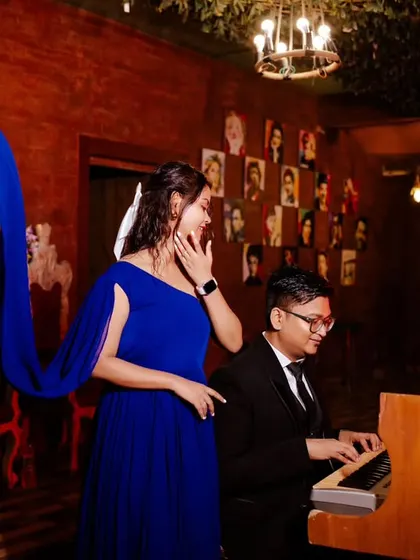A melody for his muse. This beautifully composed shot captures the groom playing the piano for his bride-to-be, with her flowing blue dress adding a touch of drama and elegance.