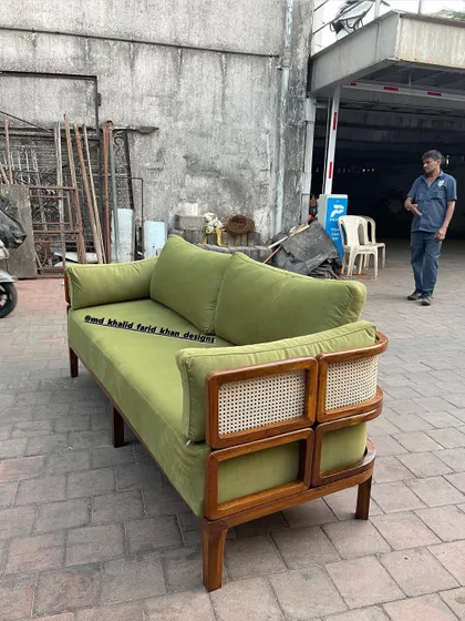 Side view of the olive green sofa, showing the elegant curve of the armrest and the detailed cane panels.