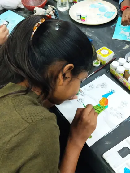 A participant painting a clay peacock mural. These workshops guide you from sculpting the base design to adding the final touches of color.