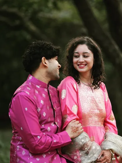 A candid photo of a couple enjoying their Mehendi function, dressed in coordinated pink outfits.