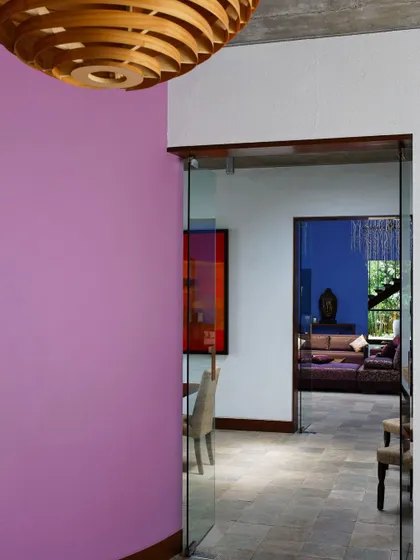 A pop of vibrant color on an accent wall provides a playful contrast to the earthy tones of the stone floor and the clear glass doors that lead into the main living area of 'The Tropical House'.