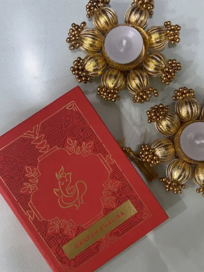 A simple yet elegant gift set for Ganesh Chaturthi, featuring a Ganesh Chalisa book and ornate golden T-light holders.