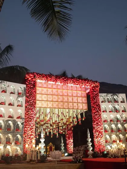 A stunning red and white floral mandap, designed with traditional arched niches. The structure looks magnificent against the evening sky, creating a truly grand setting for a wedding.