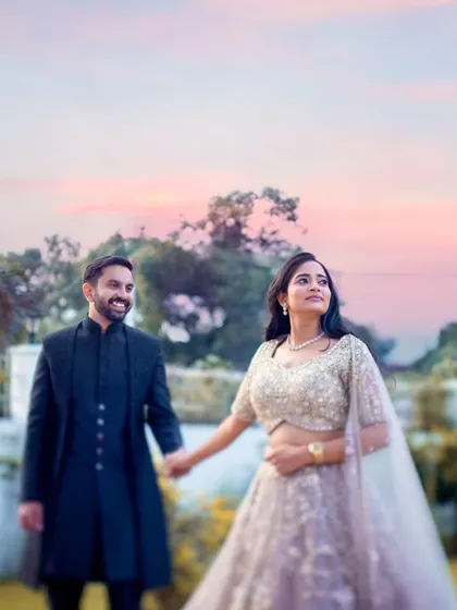 A dreamy, romantic shot of a couple holding hands in a garden at dusk, with a beautiful pink and orange sky creating a magical atmosphere.