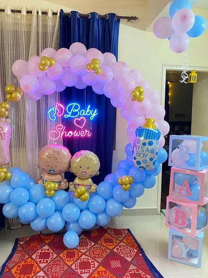 A "Baby Shower" setup with a neon sign, a pink and blue crescent-shaped balloon arrangement, and "BABY" blocks.